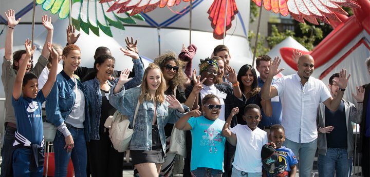 A group of people at a festival smile and hold their hands in the air to wave 